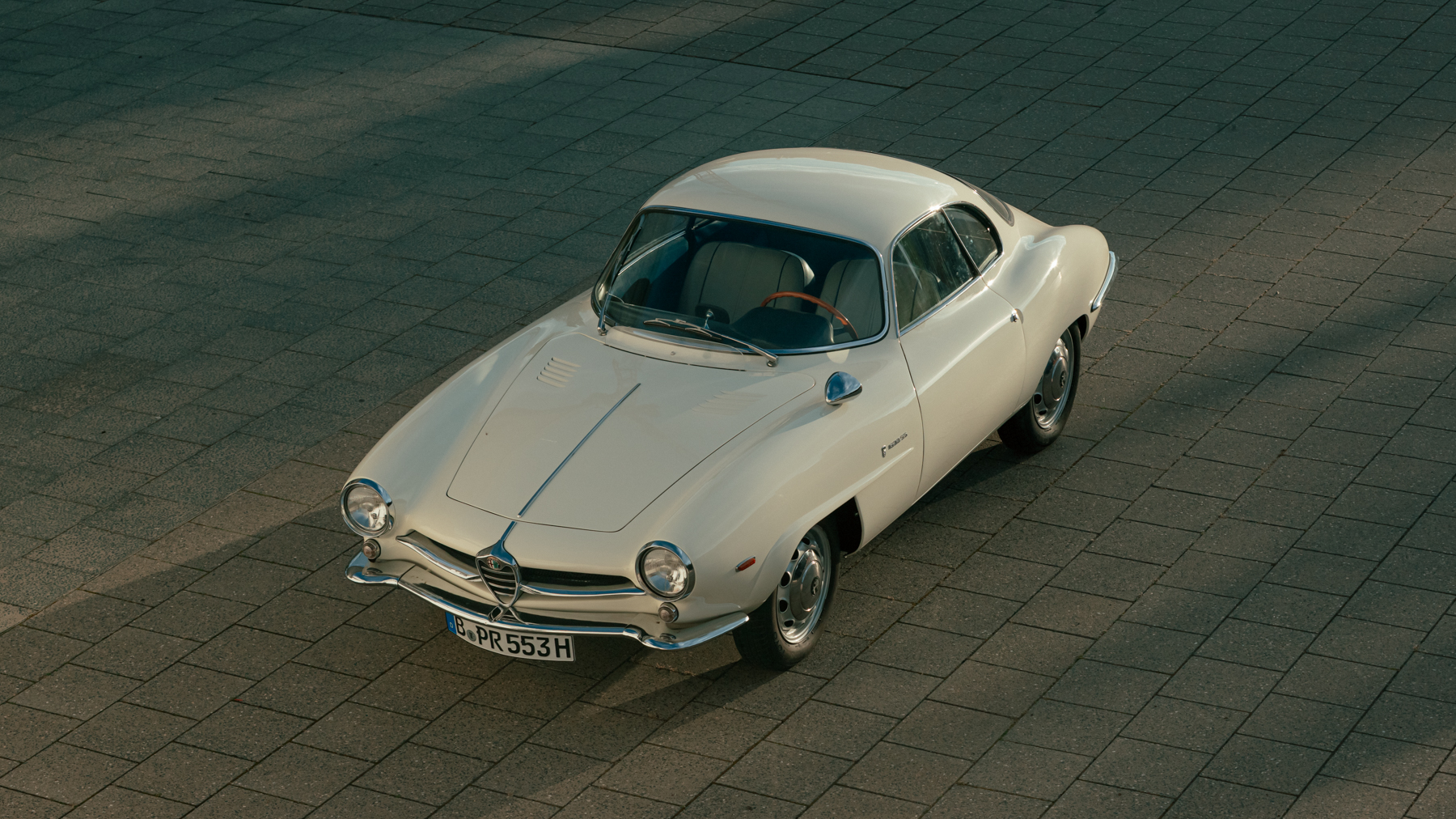Restored white Alfa Romeo Giulia 1600 Sprint Speciale parked in Berlin, showcasing its sleek, aerodynamic design and hand-crafted bodywork